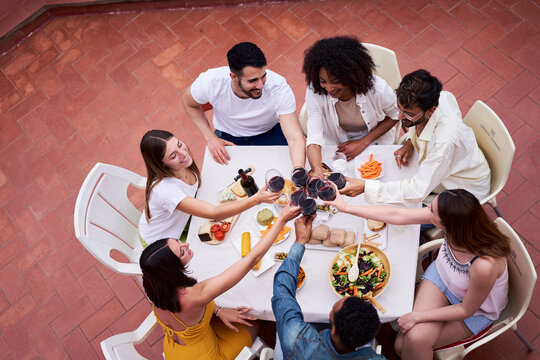 High angle view of people toasting. Happy group of Multiracial friends having dinner outside in a terrace celebrating with red wine.