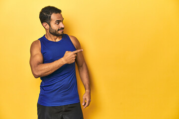 Fit Latino man in sportswear pointing to space, yellow studio background.