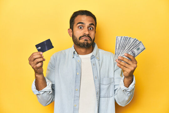 Latino man holding credit card and dollars, depicting different means of payment.