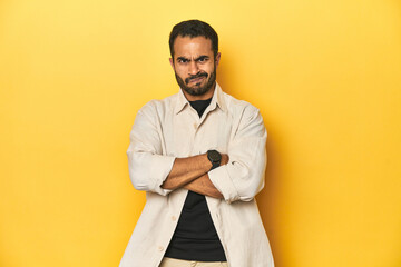 Obraz premium Casual young Latino man against a vibrant yellow studio background, frowning face in displeasure, keeps arms folded.