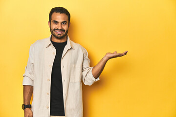 Casual young Latino man against a vibrant yellow studio background, showing a copy space on a palm...