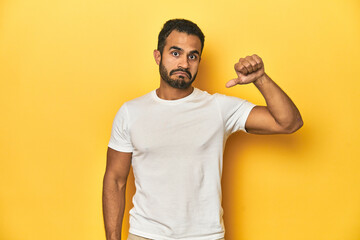 Casual young Latino man against a vibrant yellow studio background, showing a dislike gesture,...