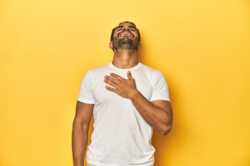 Casual young Latino man against a vibrant yellow studio background, laughs out loudly keeping hand...