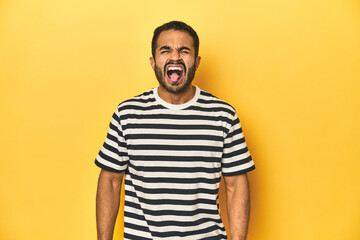 Obraz premium Casual young Latino man against a vibrant yellow studio background, funny and friendly sticking out tongue.