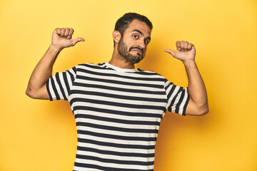 Casual young Latino man against a vibrant yellow studio background, feels proud and self confident,...