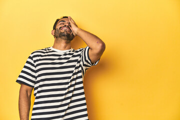 Casual young Latino man against a vibrant yellow studio background, laughing happy, carefree, natural emotion.