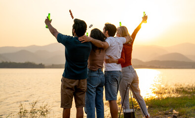 Back of group of friends with multi-ethnic hug together also hold bottle of drinking stand in front...