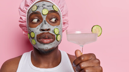 Surprised adult man showcases his enjoyment of self care rituals with fresh cocktail in hand gently...