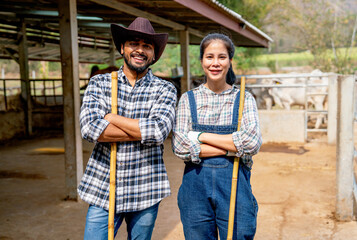 Portrait of Asian man and woman farmers carry broom and stand with arm crossed also look at camera with smiling in front of stable of cow look relax after clean the area. - obrazy, fototapety, plakaty