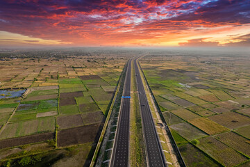 orbit aerial drone shot of new delhi mumbai jaipur express elevated highway showing six lane road with green feilds with rectangular farms