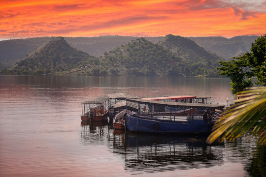 boats moored tied on Dhebar lake with Aravalli hills in the distance at dusk showing the beautiful view of asia's largest manmade lake and popular tourist and holiday destination