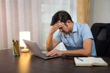 A men is exhausted due to sitting at home working and booking laptop for a long time at his desk.