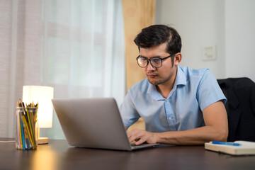 Asian young men in glasses are serious about working with laptops. via online from home.