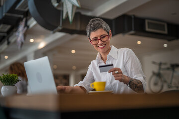 One senior woman with eye glasses holding credit card and shopping online on laptop, modern consumer concept