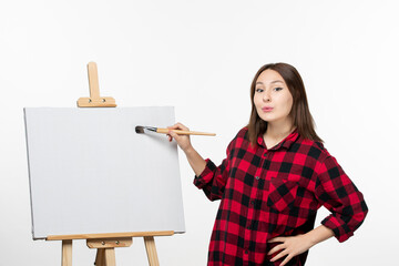 front view young female drawing with paint brush on easel on white background photo color art draw...