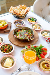 Fototapeta na wymiar Turkish breakfast table. Flat-lay of peoples hands taking pastries, vegetables, greens, olives, cheeses, fried eggs, spices, jams, honey, tea in copper pot and tulip glasses, wide composition 