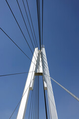 Modern urban cable-stayed bridge with metal ropes over cloudless blue sky