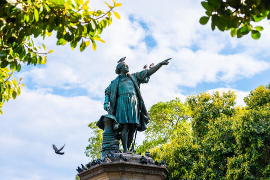 Monument to Christopher Columbus in Colonial City of Santo Domingo. Green foliage in the foreground and flying pigeons. Popular tourist landmark of the capital