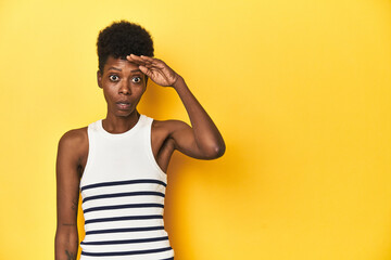 Vibrant African woman, white tank-top, yellow studio, shouts loud, keeps eyes opened and hands tense.