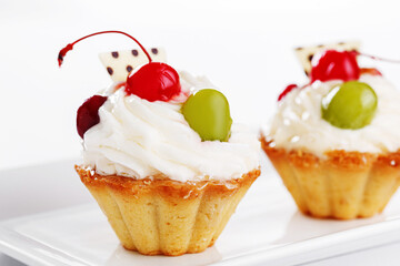 Beautiful cream cakes with cherries and grapes on a plate on a white background