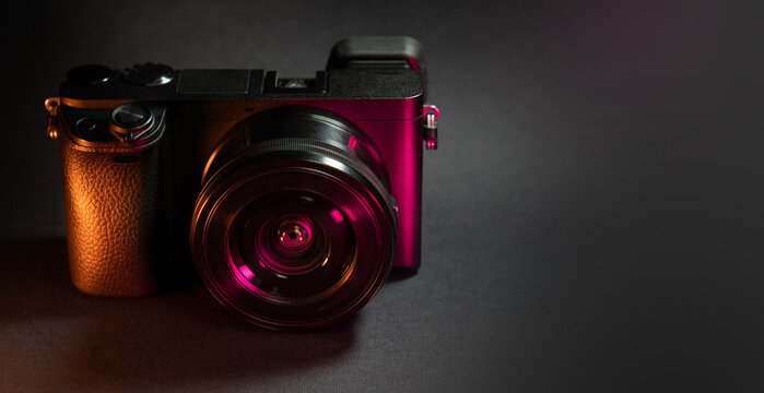 Photo camera on dark background. Neon lights. Photo gear copy space.