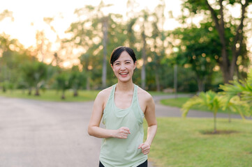 Fototapeta na wymiar Fit Asian young woman jogging in park smiling happy running and enjoying a healthy outdoor lifestyle. Female jogger. Fitness runner girl in public park. healthy lifestyle and wellness being concept