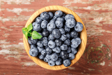 Blueberry berries with mint leaves are in a wooden plate on wooden background.