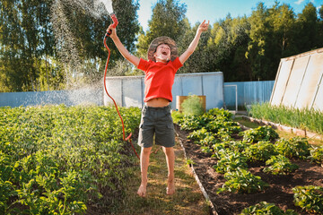 boy child jumping splashing hose water in the backyard in the garden in summer at sunset in the sunshine having fun summer