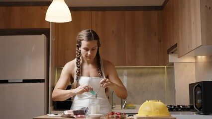A young woman with braided hair and wearing a white apron is preparing strawberries in chocolate in the kitchen. - Powered by Adobe