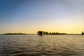 A lake at sunset with a sailboat sailing by