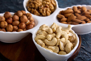 Close-up of delicious cashew nuts in a beautiful white curly dish with other nuts. Assorted roasted and dried nuts laid out close-up on a white dish