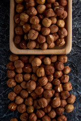 Peeled, dried, healthy hard hazelnuts are used as a snack or for baking. Dried hazelnuts, fried in a square wooden bowl on a gray textured background