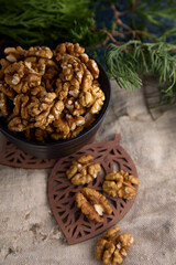Top view of deep black bowl filled with halves of peeled walnut, against background of an old burlap and green coniferous branch. Nutritious healthy tasty walnut in a bowl on burlap fabric background