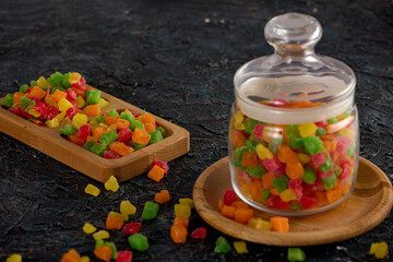 Beautiful colored candied fruit is laid out in a wooden bowl and in a glass jar on the table. Healthy delicious snack of dried fruit on a black textured table in a wooden dish