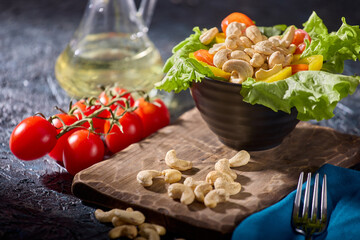 Dried cashew nuts, along with fresh vegetables, are beautifully laid out on a dark textured table and dishes. Beautiful serving of healthy vegetables and nuts for a hearty vitamin breakfast