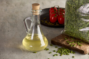 Vegetable oil in a glass carafe is on the table next to a plate of tomatoes and peeled pumpkin seeds in a transparent bag. Useful vitamin products for health