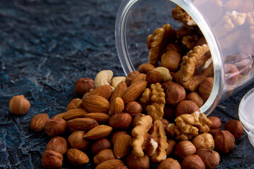 Close-up on a gray table is an open jar with a scattering of nut mix from different nuts. A blend of delicious, nutritious, healthy nuts for a healthy diet is stored in a glass jar