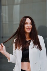
beautiful young woman in a white jacket and black trousers with an open belly and a tattoo in the city against the backdrop of glass buildings