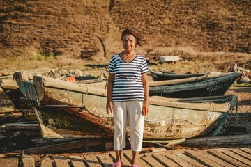 an elderly woman sailor on the seashore against the backdrop of boats enjoys the breeze and freedom