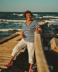 an elderly woman sailor on the seashore against the backdrop of boats enjoys the breeze and freedom