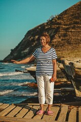 an elderly woman sailor on the seashore against the backdrop of boats enjoys the breeze and freedom