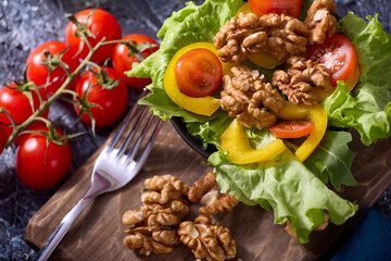 Halves of peeled walnuts along with fresh, bright, delicious vegetable cuts on a gray background. Cherry tomatoes and healthy walnuts are on the table in a black dish along with a fork