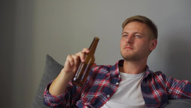 A young man drinking beer while sitting on the couch. Concept of free time, sport and entertainment
