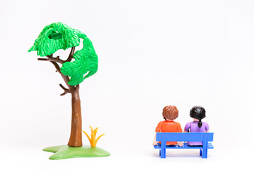 Couple of people, a man and a woman, sit on a bench under a tree, view from the back