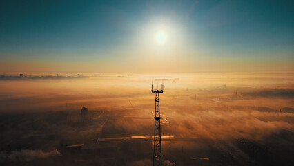 Landscape from drone. Sun on horizon line and fog over industrial industrial zone. Communication tower against sky. Beautiful dawn. - Powered by Adobe