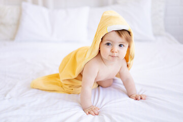 a baby girl of six months on a bed with a yellow towel on her head after bathing or washing, a...