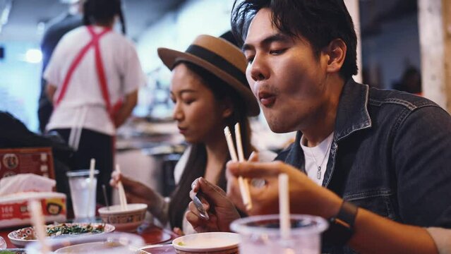 Young Asian couple traveler tourists eating Thai street food together in China town night market in Bangkok, Thailand