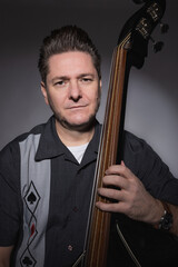 Vertical studio portrait of a 40 years old male musician playing the double bass rockabilly style