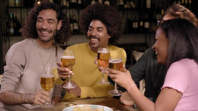 Group of hispanic people partying and drinking beer in a pub. Young multiracial friends having fun in a bar. They chat and laugh. The African American woman looking at camera