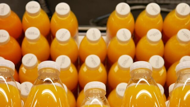 Close-up of many orange juice bottles on a mirrored display case and a male buyer hand takes one